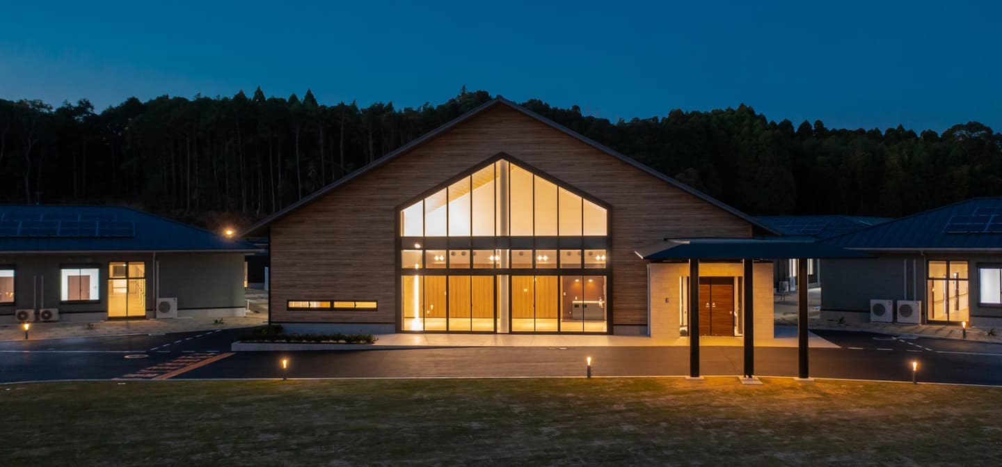 夜間にライトアップされた現代的な介護施設の建物外観。大きな窓と木製の外壁が特徴。
